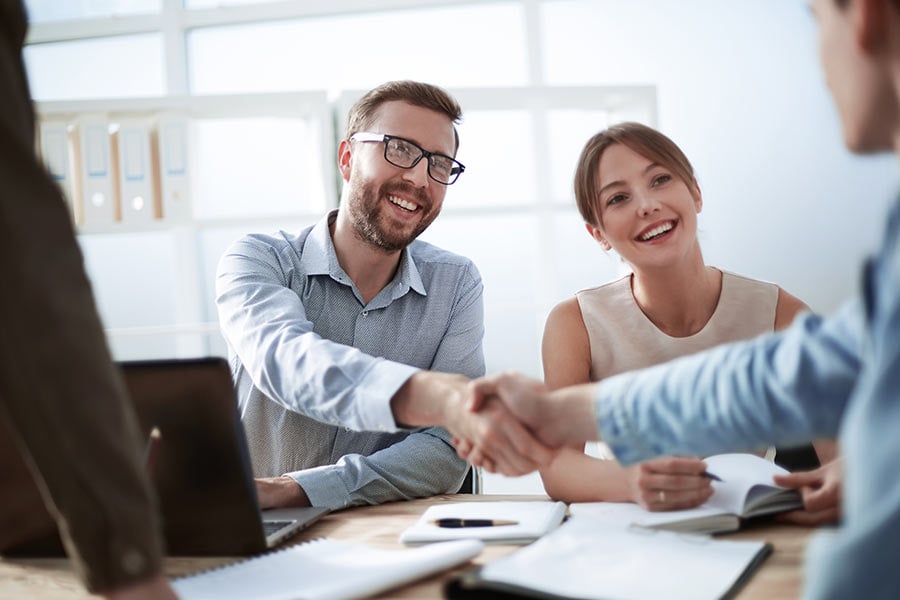 Businesspeople collaborating at a desk, shaking hands.