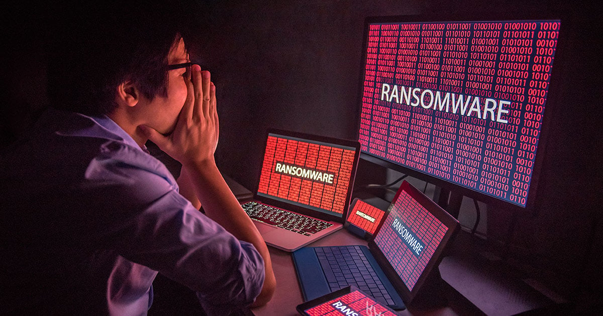 Man frustrated, confused and headache by ransomware attack on desktop screen, notebook and smartphone