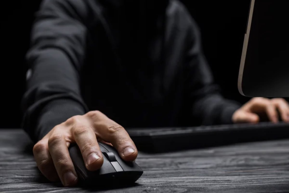 a man in a hoodie working on a computer with one hand on the mouse