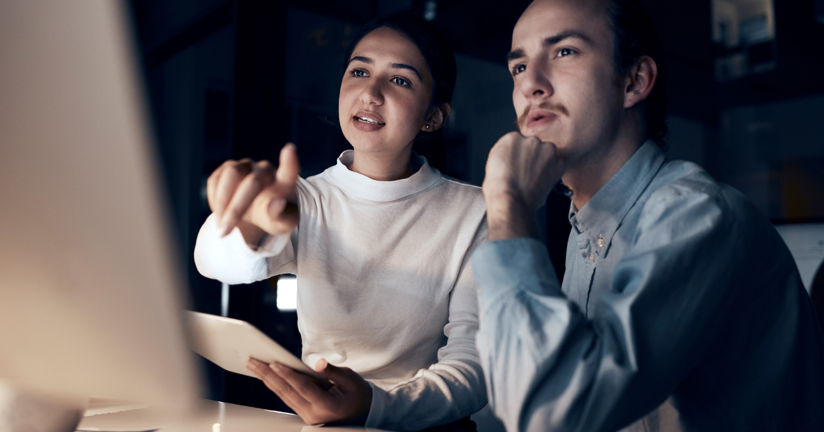 Two people sitting together at a table looking at a desktop computer screen.