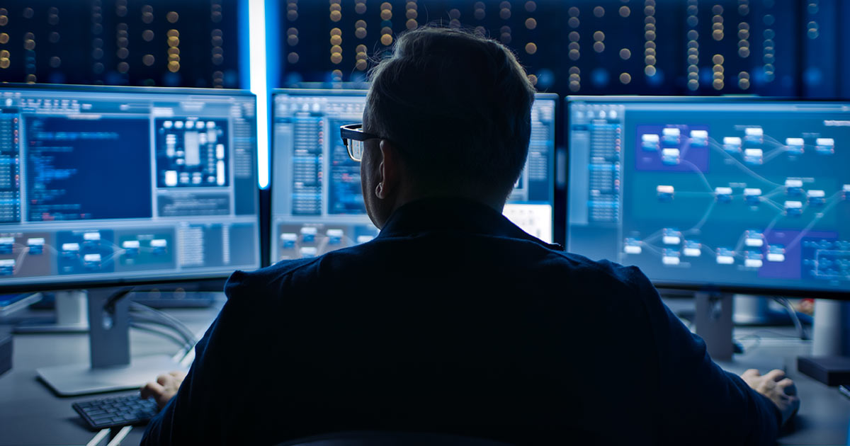 Professional cybersecurity expert in front of three computer screens