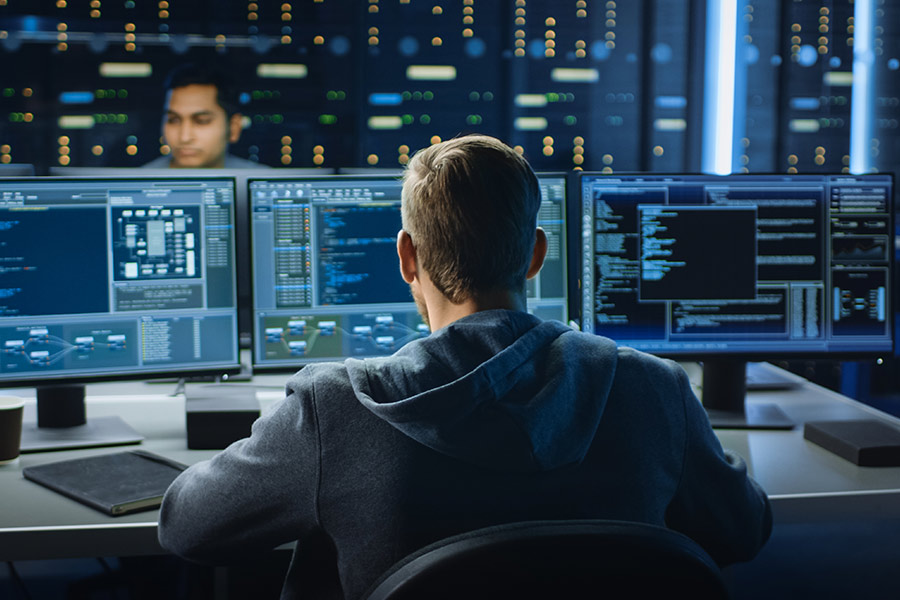 Cybersecurity technician facing three computer monitors