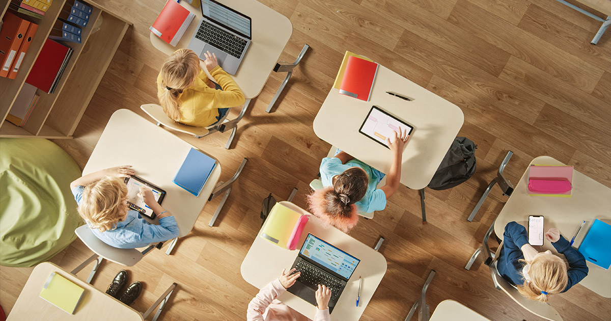 top view shot of children sitting at their school desks using computers, tablets, or phones