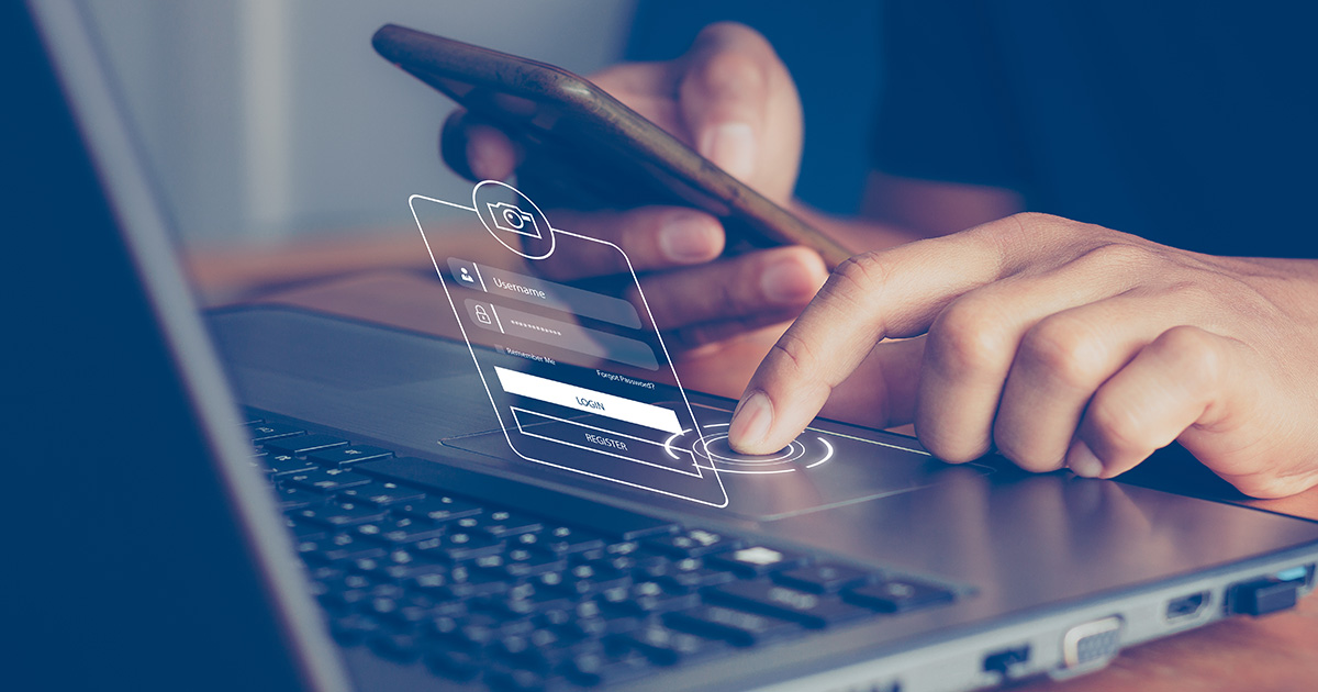 closeup of man with left hand typing on laptop while right hand checks his phone